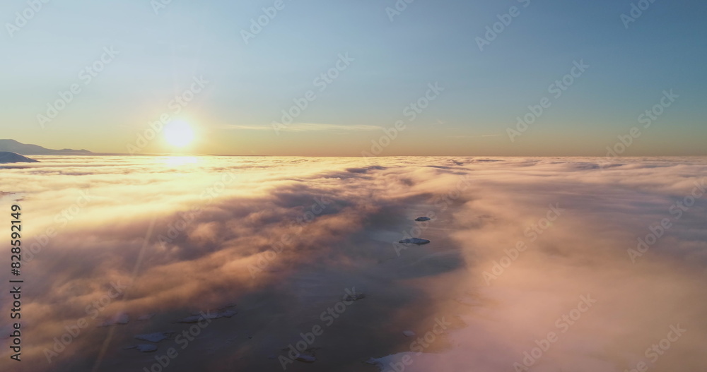 Aerial high altitude flight over morning cloudscape. Sunrise sun shine on bright layers of fluffy clouds, arctic ocean water and mountain range peaks. Nature background perfect landscape wallpaper