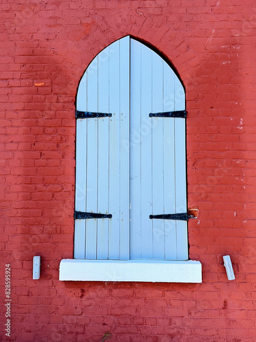 The closed blue wooden shutters of a window set in a bright red brick wall of Fisgard Lighthouse. photo