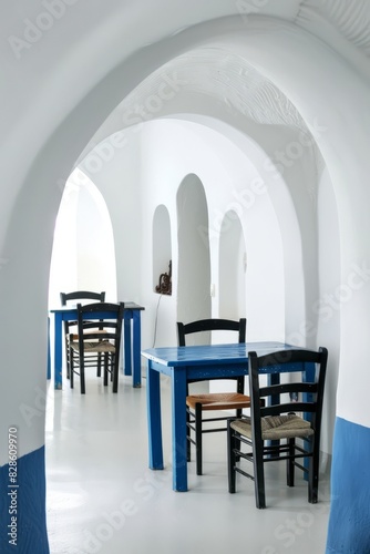 On white walls, there is a blue table and chair in the center of the room, and arches lead to other rooms. There are white archways in the doorway and dark wooden furniture in the other rooms. © SHI