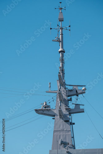 Closeup of a mast and antennas on a warship agains a bright blue sky.