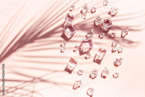Ice cubes and palm leaves on a pink background with contrasting shadows. Flat lay
