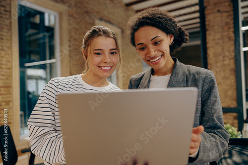 Smiling female business people standing in an office and using a laptop together