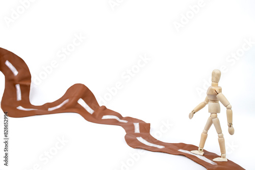 Wooden mannequin walking on a brown leather wavy road, journey to a goal concept, close up isolated on white © Dorin
