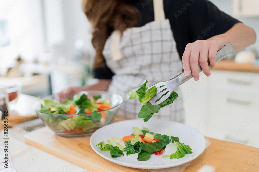 Closeup hands of young asian woman using tongs to take salad into the plate after mixing fresh vegetables salad in bowl and cooking healthy breakfast food in kitchen with healthy lifestyle at home Closeup hands of young asian woman using tongs to take salad into the plate after mixing fresh vegetables salad in bowl and cooking healthy breakfast food in kitchen with healthy lifestyle at home