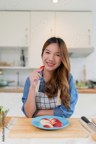 Young asian woman enjoying and eating slices apple while preparing fruits and fresh vegetables salad to cooking healthy breakfast food for homemade snack in kitchen with healthy lifestyle at home