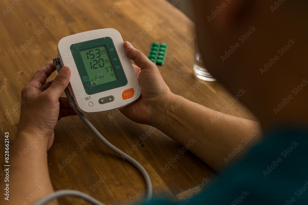 Seniory man checks blood pressure with monitor on upper arm in room Seniory man checks blood pressure with monitor on upper arm in room