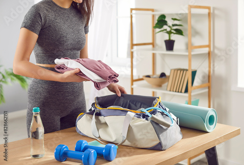 Fototapeta Naklejka Na Ścianę i Meble -  Close up shot of a woman packing a sport bag with equipment and sportswear on table at home. Preparing for a active gym workout, planning fitness and gymnastics or aerobics activities.