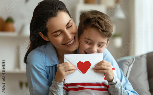 A mother and son are hugging each other, the boy holding an envelope with a heart symbol on it in his hand