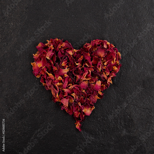 Dried red rose petals in heart shape lie on stone surfase. Design element. Dry rose petals used in alternative medicine and aromatherapy