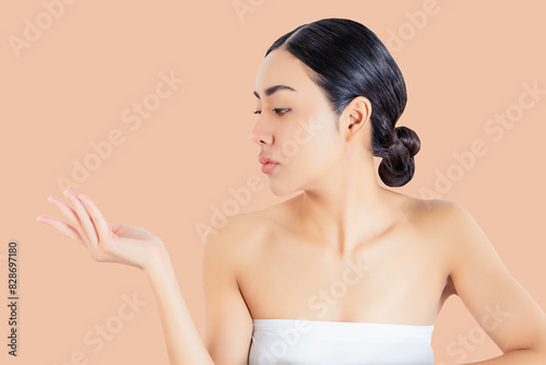 A young woman with smooth, glowing skin poses against a peach-colored background. She is looking at her open hand with a serene expression. Her hair is neatly tied back, emphasizing her natural beauty