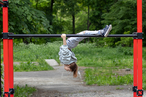 A fitness girl hangs upside down on a horizontal bar in a street gym. Outdoor fitness