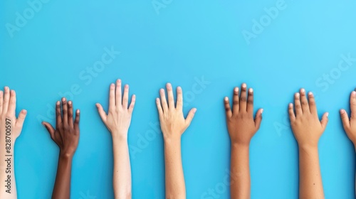 Colorful cut out paper hands of different skin colors reaching up on a blue background.