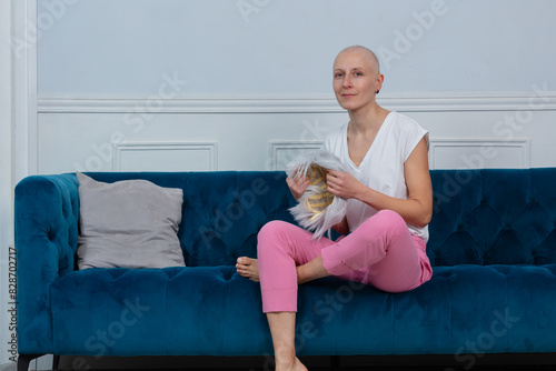 Bald woman cancer fighter hold wig sits in hands on blue sofa