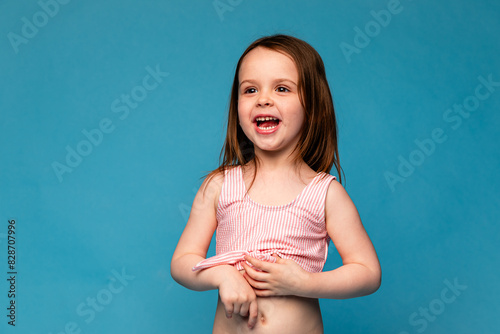 Happy little girl in a pink swimsuit laughs cheerfully. Mockup. Isolated blue background. Summer vacation concept. Place for text