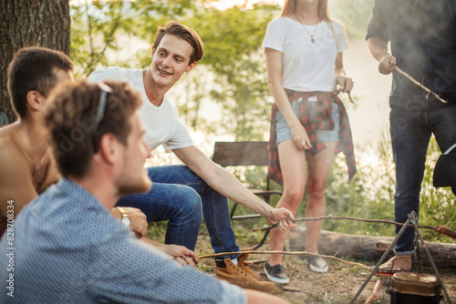 handsome smiling man in T-shirt and jeans is sitting with stick among friends. close up cropped photo