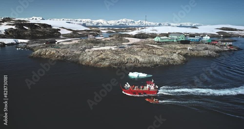 People travel to Antarctica. Explore South Pole. Tourists on red boat zodiac sailing polar ocean enjoy wild nature ocean landscape with snow covered mountains. Tourism expeditions. Aerial drone shot