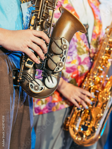 Musician playing saxophone on blurred background. Man with friends blow saxophone with the band for performance. Music instrument played by saxophonist player musician in festival. Selective focus.