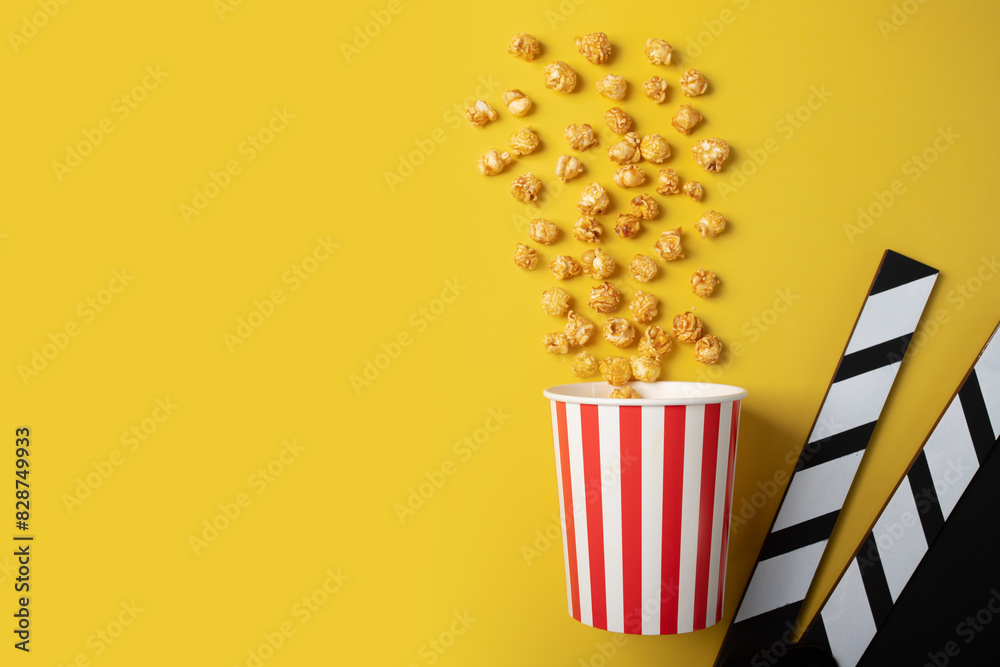 Popcorn caramel bucket and Cinema clapper board, movie theater snack, film production treat, Hollywood cinema night,yellow background, copy space