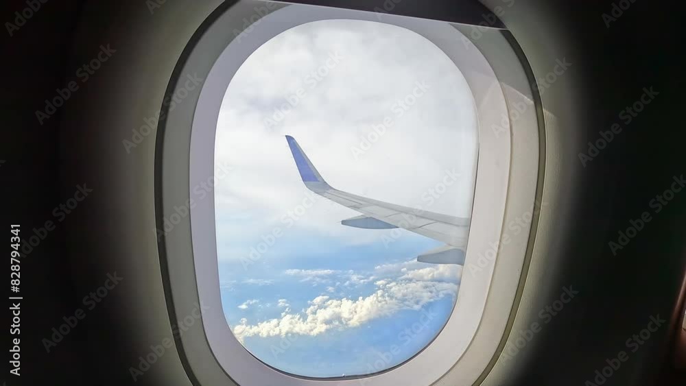 View of airplane wings in clouds through porthole. Blue sky background. Beautiful clouds and airplane wings from the window with beautiful blue sky