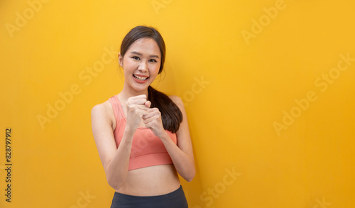 Portrait of healthy and slim Asian athlete woman in sportswear smiling on the isolated yellow background for exercise and workout concept