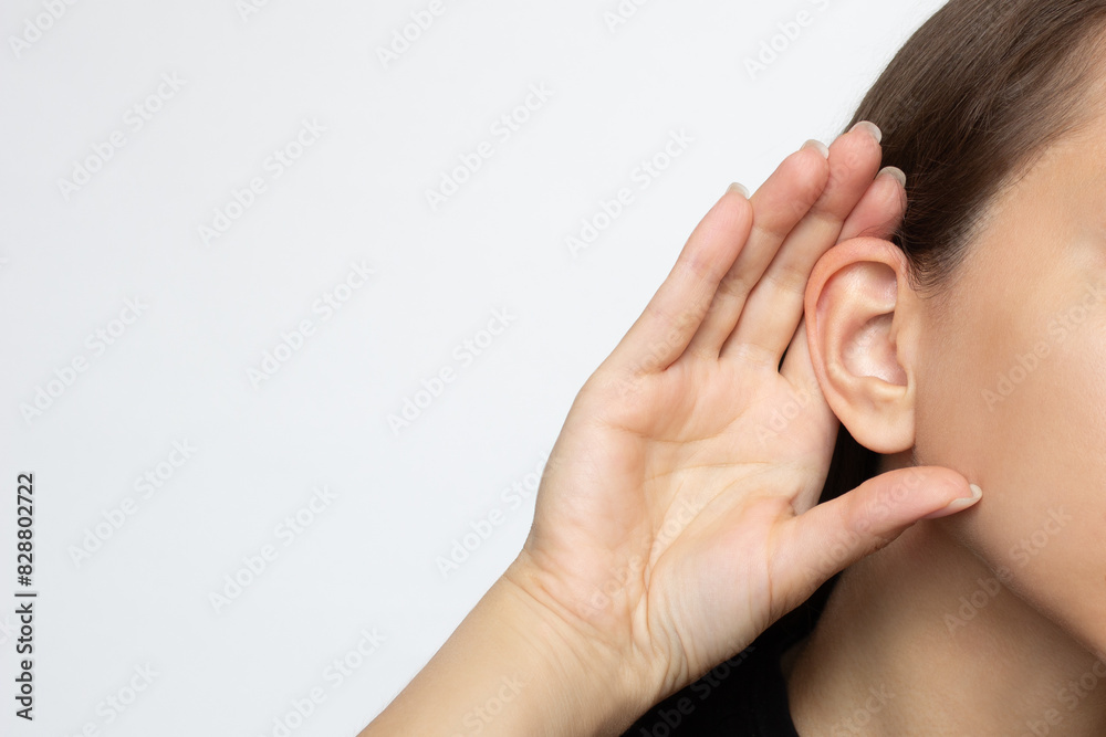 A woman puts her hand to her ear and listens, isolated on a white background with copy space. Hearing problems, ear diseases, noise. Concept of testing and hearing loss, audiometry A woman puts her hand to her ear and listens, isolated on a white background with copy space. Hearing problems, ear diseases, noise. Concept of testing and hearing loss, audiometry