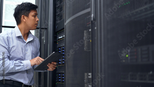 A technician in a blue shirt uses a tablet while inspecting a server rack in a modern data center, ensuring proper functionality.