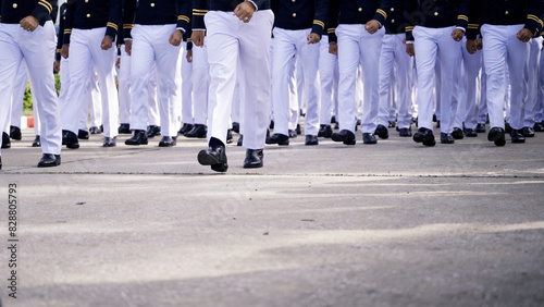 A group of cadets dressed in formal uniforms, marching in synchronized formation on a paved road during a military parade or drill.