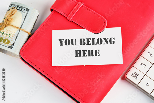 Diversity, business, inclusion and belonging concept. You belong here symbol on a business card on a business notebook near money and a calculator on a white background