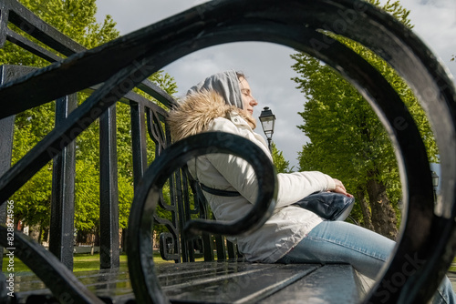 woman in white coat relaxing in a park on a bench