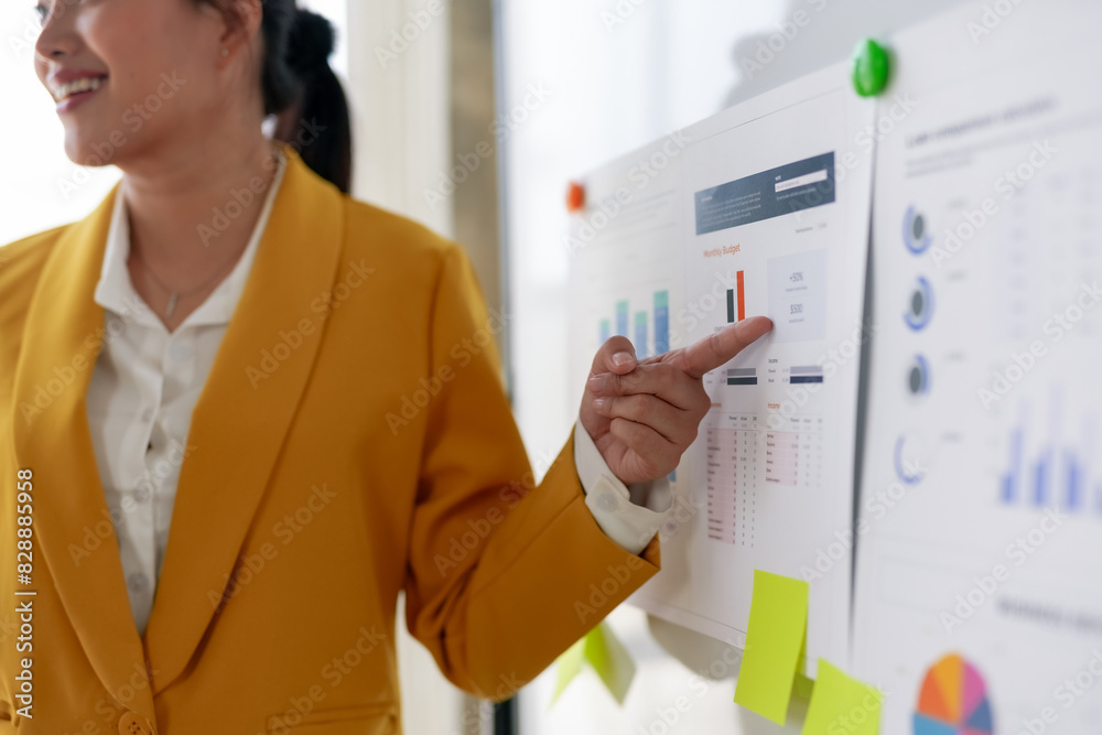 Businesswoman presenting data on a whiteboard in an office setting. Focus on growth charts, statistics, and business analysis.