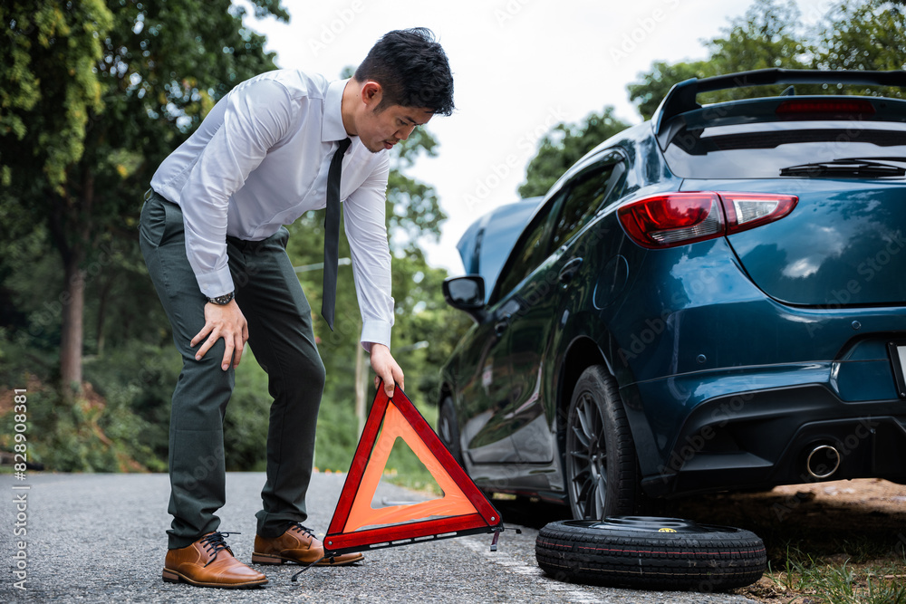 Man having car trouble and stranded at roadside with red warning triangle behind his broken car. Waiting for emergency assistance and transportation services. Man having car trouble and stranded at roadside with red warning triangle behind his broken car. Waiting for emergency assistance and transportation services.