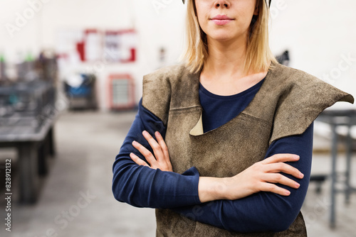 Beautiful blonde woman works as a welder in workshop, wearing leather welding apron. photo