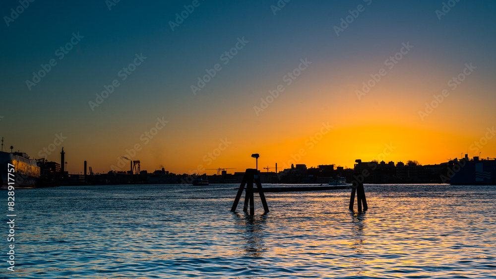 Fototapeta premium Golden sunset and city silhouette by a river.