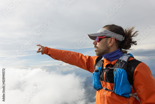 A man in an orange jacket pointing to the sky photo