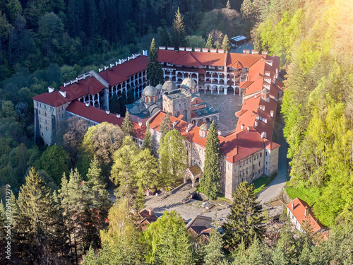Aerial view of the iconic Rila Monastery, showcasing its red-tiled roofs, intricate architecture, and surrounding lush green forest, Rila Mountains, Bulgaria. Orthodox Christian complex, UNESCO site.
