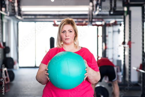 Portrait of overweight woman exercising in gym, holding medicine ball