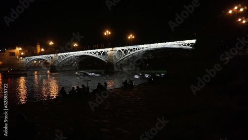 Bridge crossing a navigable river in a city at night on whose bank you can see silhouettes of people photo