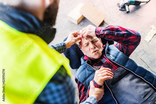 Cuadro en lienzo Colleague calling ambulance and giving first aid to injured worker, in pain after accident at construction site Concept of occupational safety and health in workplace