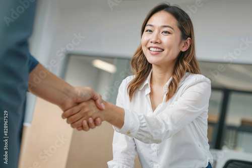 Asian woman shakes hands with a man in a business setting she is smiling and she is happy. Contract signing concept