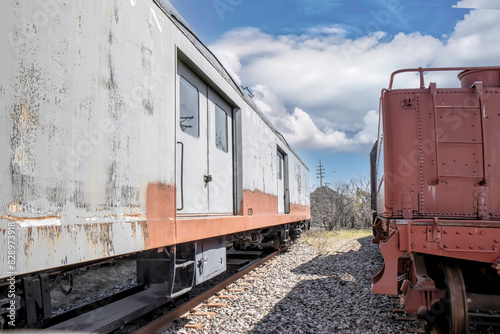 Two older railcars sitting at the end of a siding, daytime, sunny, nobody
