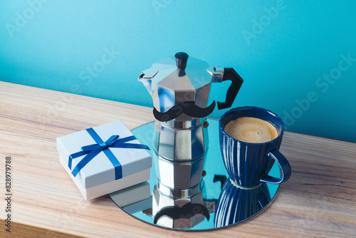 Happy Father's day concept with coffee maker, coffee cup, gift box and mirrored tray on wooden table over blue background