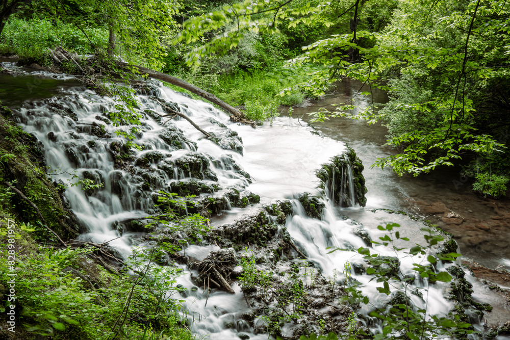 Fototapeta premium Long Exposure. Surrounded by bright green spring foliage and ferns, waterfall in Bulgaria. cascades over the rocks. Side view.