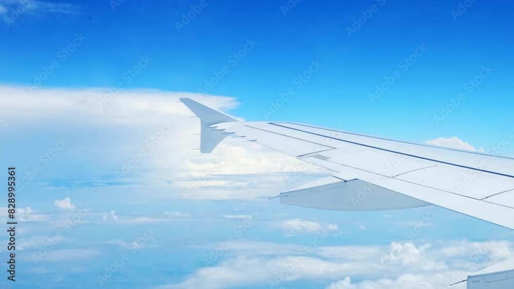View of an airplane wing from a porthole against a blue sky background. A passenger plane flies above the clouds in the morning light. The concept of traveling by air. Fear of heights, aerophobia. 4K View of an airplane wing from a porthole against a blue sky background. A passenger plane flies above the clouds in the morning light. The concept of traveling by air. Fear of heights, aerophobia. 4K