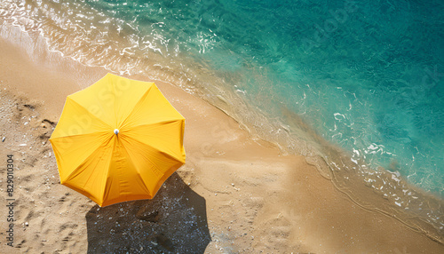 Yellow beach umbrella on sandy coast near sea, top view