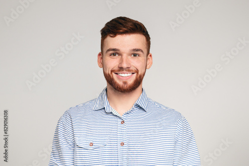 Portrait of smiling bearded millennial guy wearing casual shirt posing isolated on beige studio background