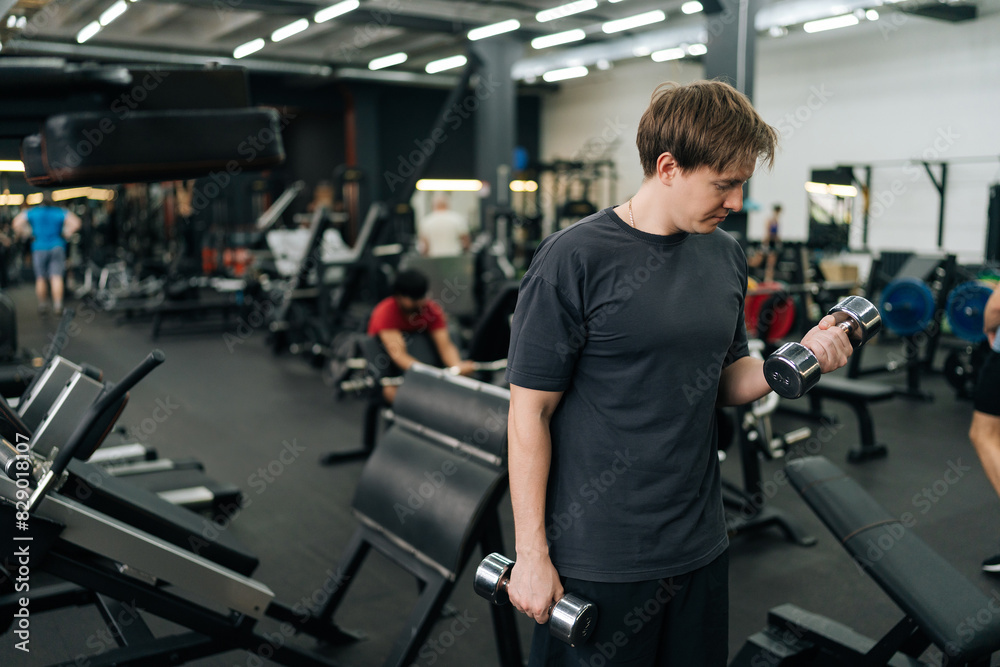 Medium shot of beginner sportsman doing exercises with weight at gym. Athletic male performing functional training with dumbbells to tone muscles. Concept of healthy lifestyle, physical sport activity