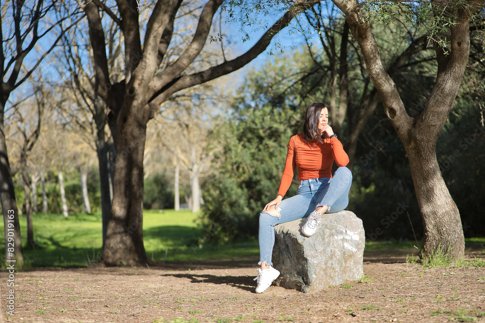 Young, beautiful woman in orange t-shirt and jeans, eyes closed, overwhelmed and stressed, sitting on a huge stone in a park. Concept fashion, beauty, problems, stress. Young, beautiful woman in orange t-shirt and jeans, eyes closed, overwhelmed and stressed, sitting on a huge stone in a park. Concept fashion, beauty, problems, stress.
