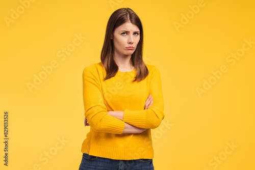 Offended, beautiful woman with arms crossed looking at camera standing isolated on yellow background
