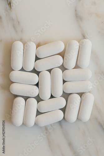 arranged grid of white pills, vitamins on white marble background