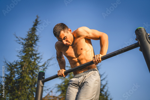 One man muscular male athlete training pull ups outdoor in sunny day